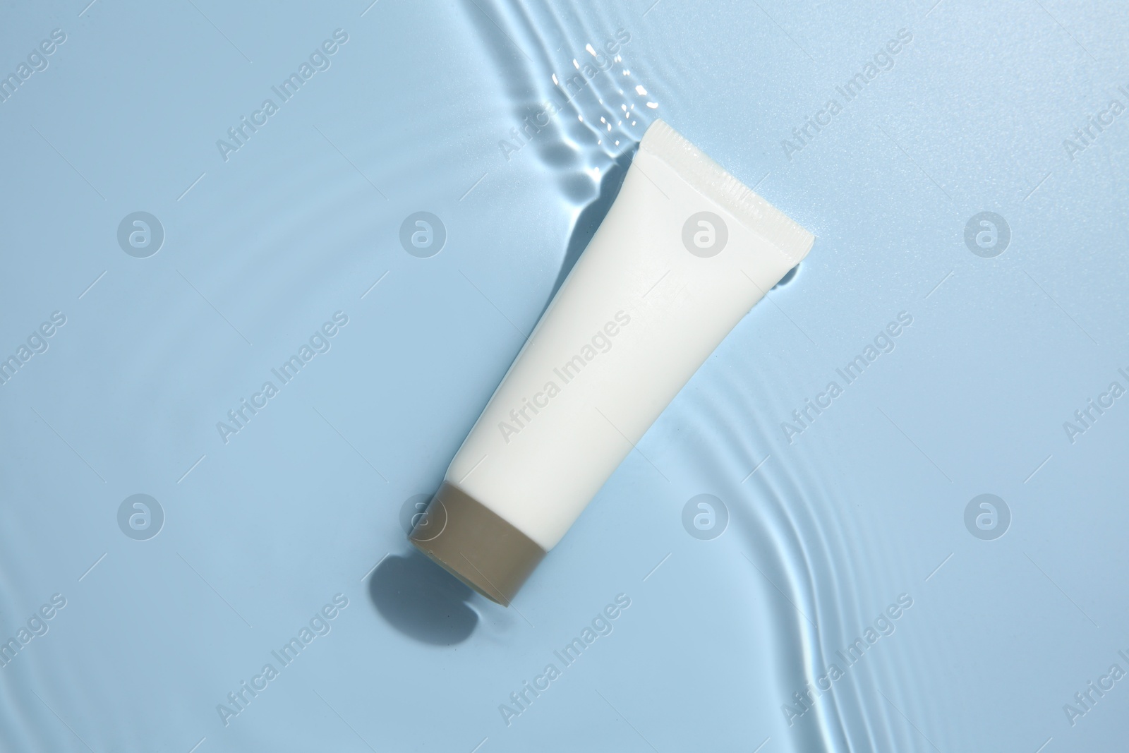 Photo of Cosmetic product. Tube with cream in water on light blue background, top view