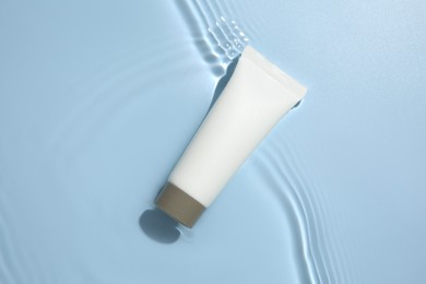 Cosmetic product. Tube with cream in water on light blue background, top view