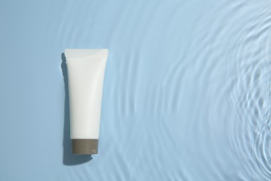 Photo of Cosmetic product. Tube with cream in water on light blue background, top view. Space for text