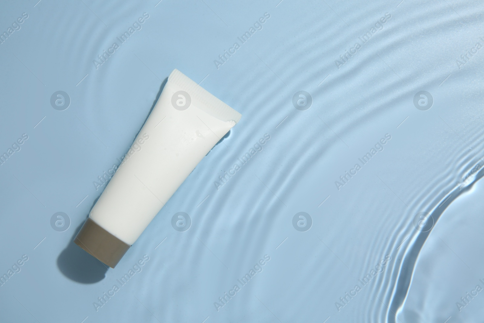 Photo of Cosmetic product. Tube with cream in water on light blue background, top view. Space for text