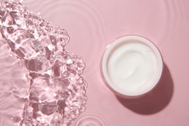 Photo of Cosmetic product. Jar with cream in water on pink background, top view. Space for text