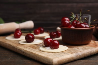 Photo of Process of making dumplings (varenyky) with cherries. Raw dough and ingredients on wooden table, closeup