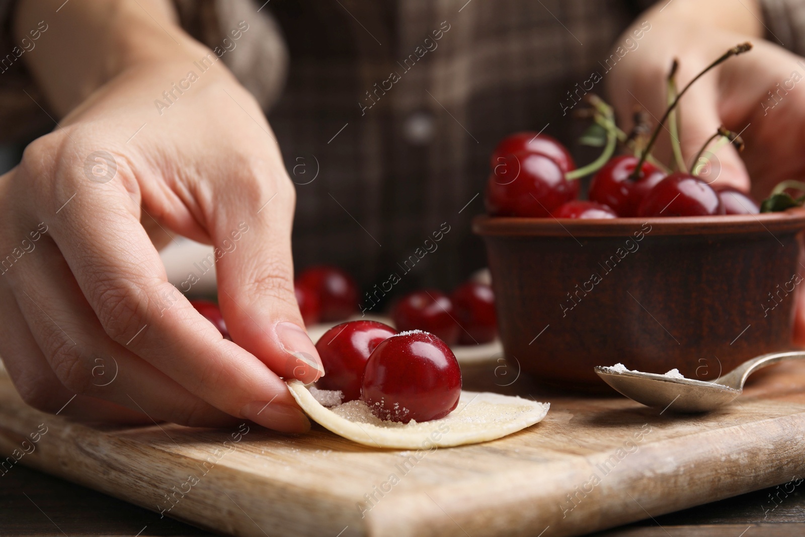 Photo of Woman making dumplings (varenyky) with cherries at wooden table, closeup