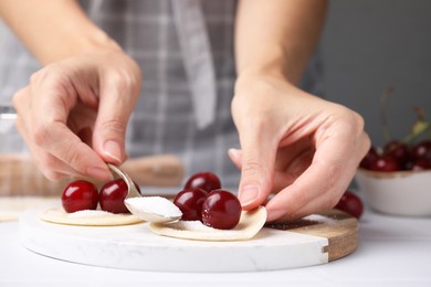 Photo of Woman making dumplings (varenyky) with cherries at white table, closeup