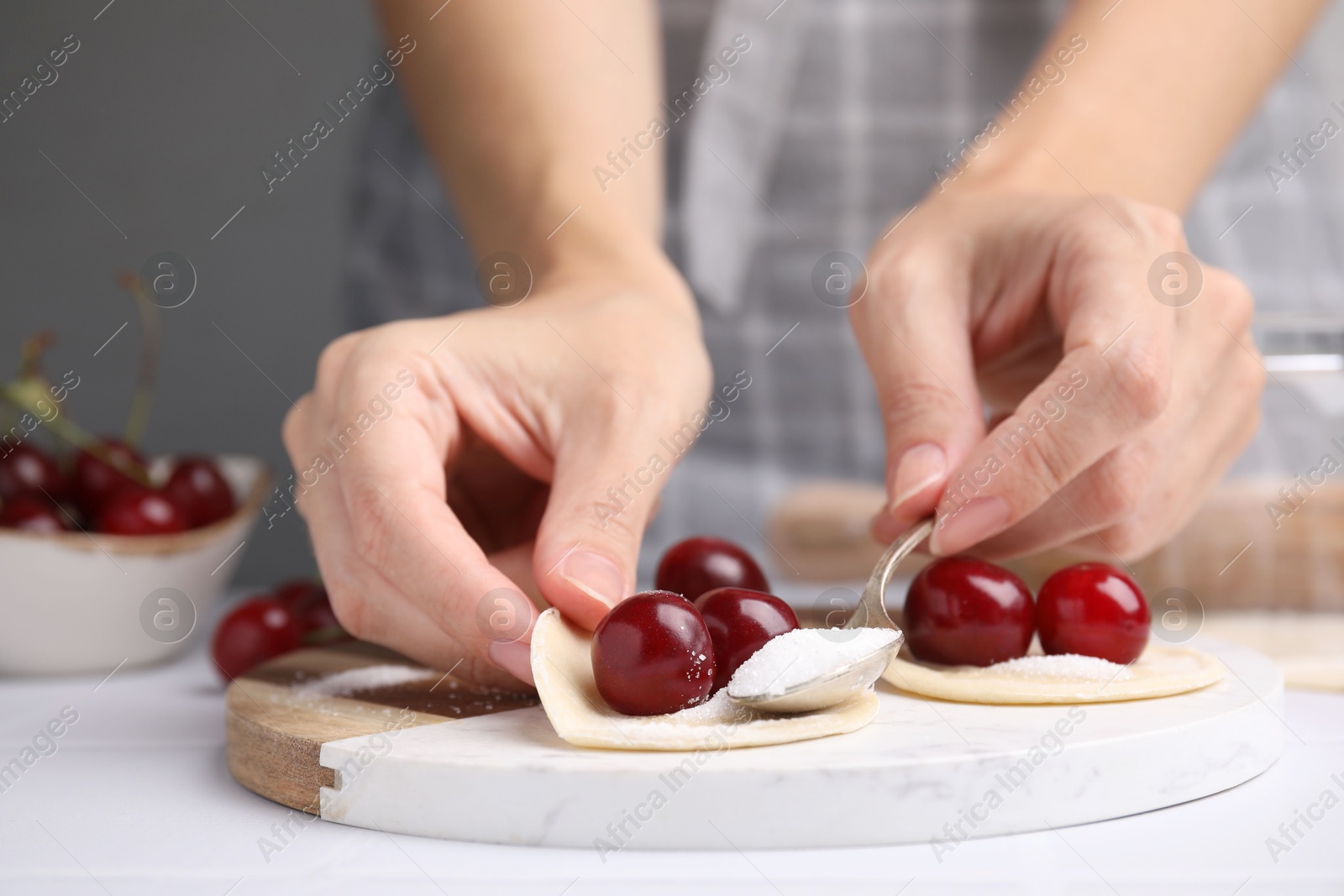 Photo of Woman making dumplings (varenyky) with cherries at white table, closeup