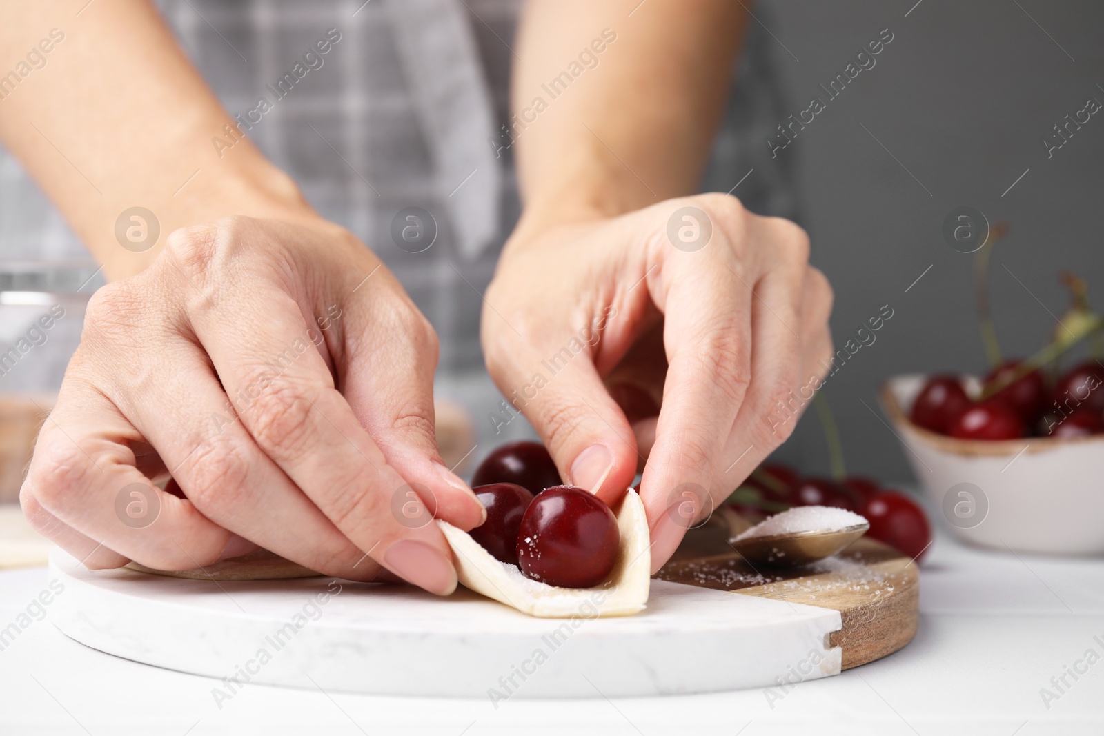 Photo of Woman making dumplings (varenyky) with cherries at white table, closeup