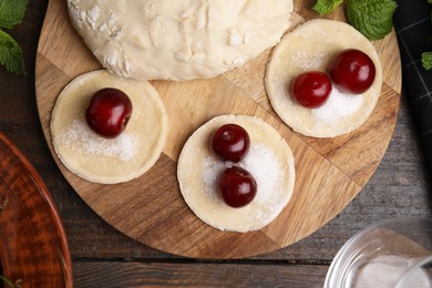 Photo of Process of making dumplings (varenyky) with cherries. Raw dough and ingredients on wooden table, flat lay