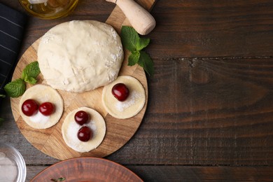 Photo of Process of making dumplings (varenyky) with cherries. Raw dough and ingredients on wooden table, flat lay. Space for text