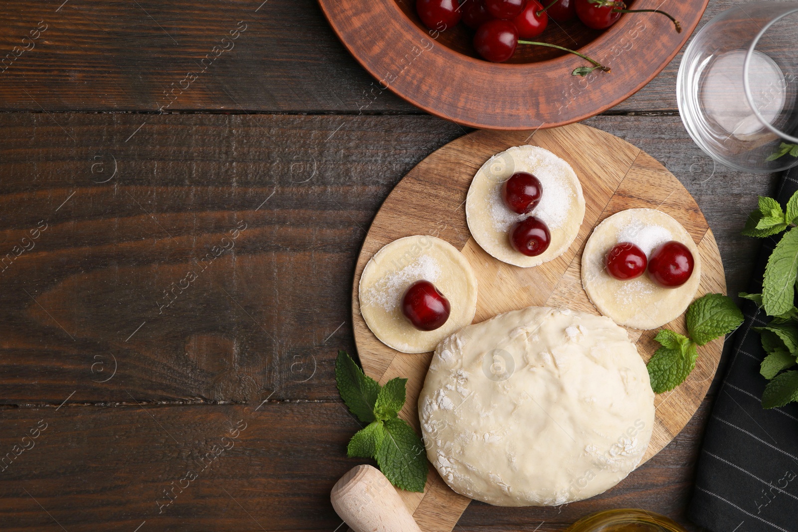 Photo of Process of making dumplings (varenyky) with cherries. Raw dough and ingredients on wooden table, flat lay. Space for text