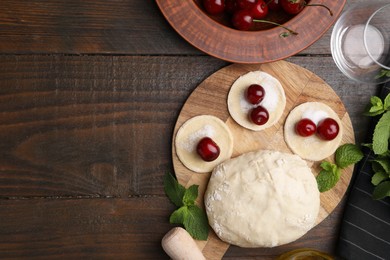 Photo of Process of making dumplings (varenyky) with cherries. Raw dough and ingredients on wooden table, flat lay. Space for text