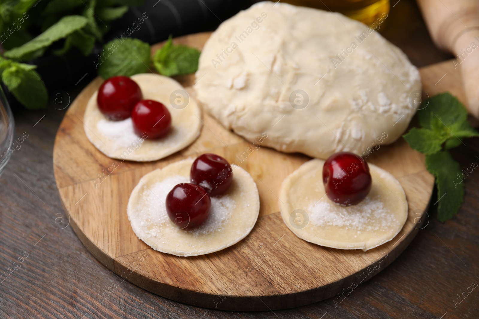 Photo of Process of making dumplings (varenyky) with cherries. Raw dough and ingredients on wooden table