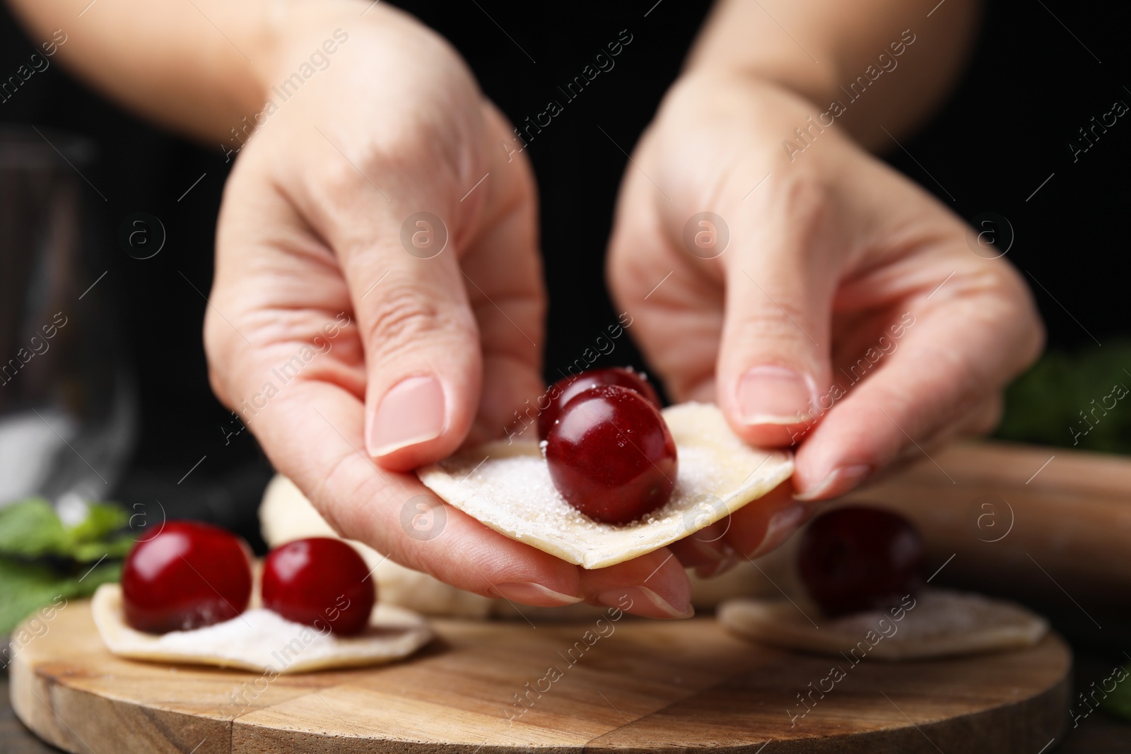 Photo of Woman making dumplings (varenyky) with cherries at wooden table, closeup