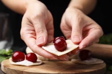 Woman making dumplings (varenyky) with cherries at wooden table, closeup