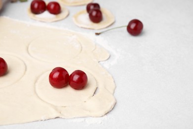 Photo of Process of making dumplings (varenyky) with cherries. Raw dough and ingredients on light table, closeup. Space for text