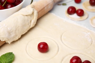 Photo of Process of making dumplings (varenyky) with cherries. Raw dough and ingredients on light table, closeup