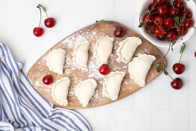 Raw dumplings (varenyky) and fresh cherries on white tiled table, flat lay