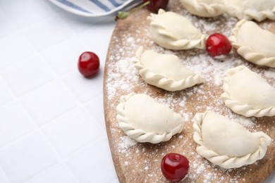 Raw dumplings (varenyky) and fresh cherries on white tiled table, closeup