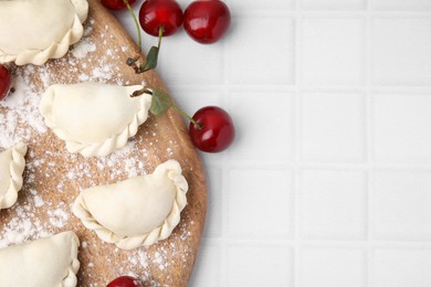 Raw dumplings (varenyky) and fresh cherries on white tiled table, flat lay. Space for text