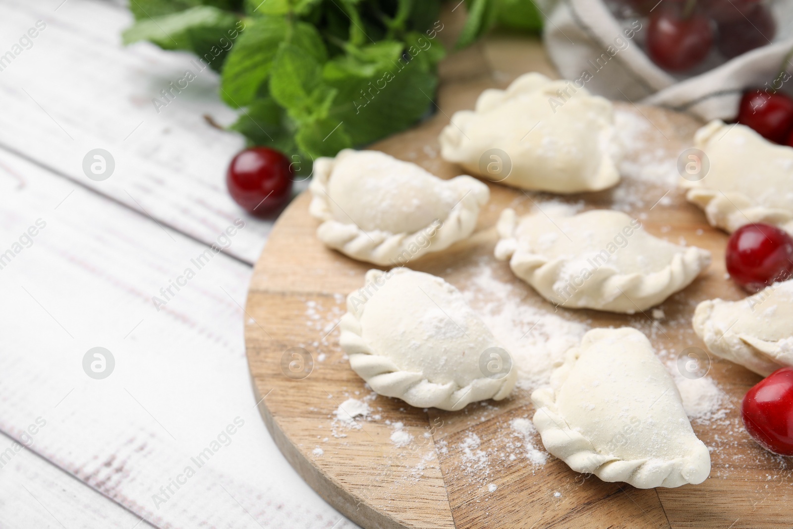 Photo of Raw dumplings (varenyky) and fresh cherries on white wooden table, closeup