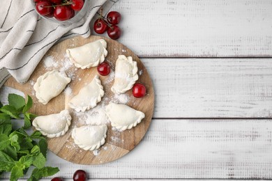 Raw dumplings (varenyky) and fresh cherries on white wooden table, flat lay. Space for text