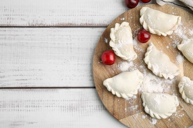 Photo of Raw dumplings (varenyky) and fresh cherries on white wooden table, top view. Space for text