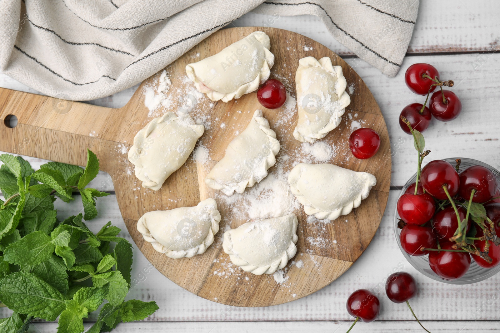 Photo of Raw dumplings (varenyky) and fresh cherries on white wooden table, flat lay