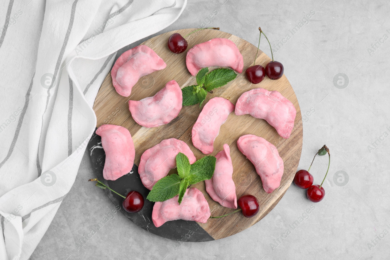 Photo of Raw dumplings (varenyky), fresh cherries and mint on grey table, flat lay