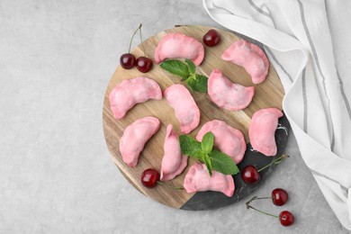 Photo of Raw dumplings (varenyky), fresh cherries and mint on grey table, flat lay