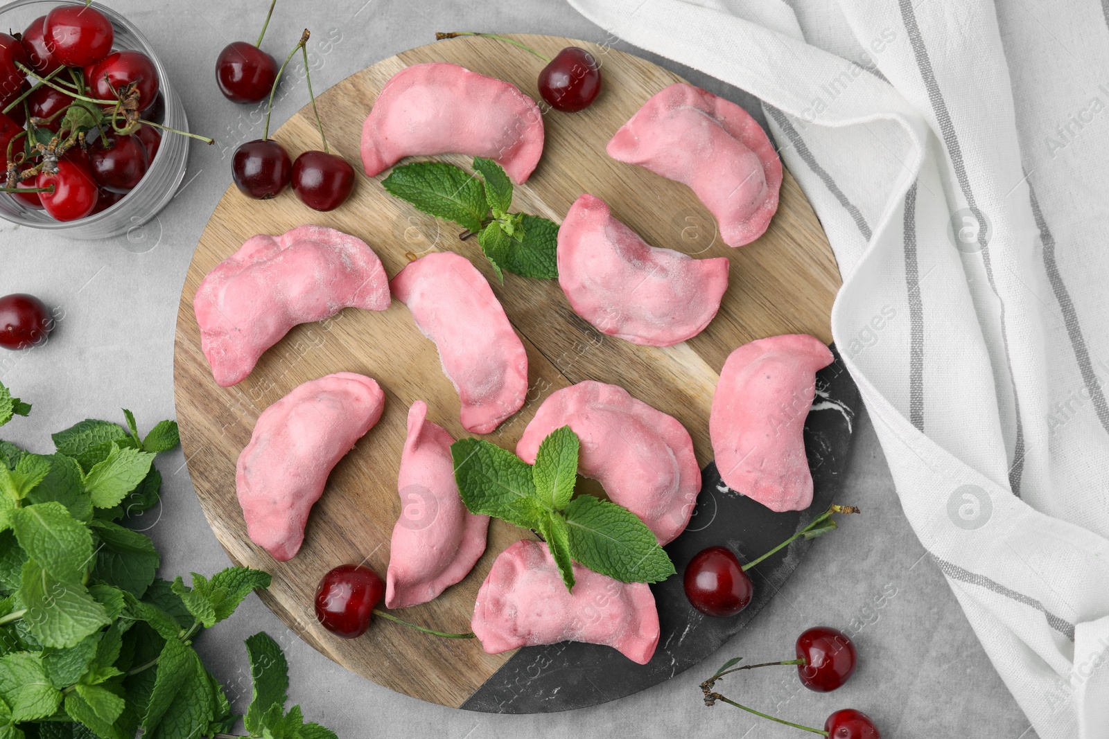 Photo of Raw dumplings (varenyky), fresh cherries and mint on grey table, flat lay