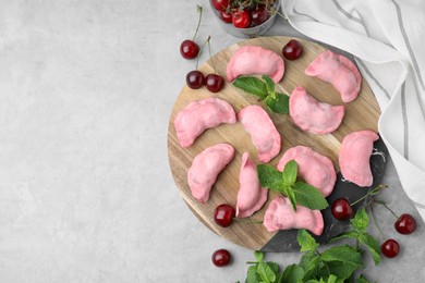 Raw dumplings (varenyky), fresh cherries and mint on grey table, flat lay. Space for text