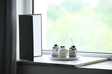 Photo of Cupcakes and light reflector on window sill in studio. Professional food photography