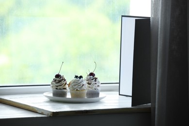 Photo of Cupcakes and light reflector on window sill in studio. Professional food photography