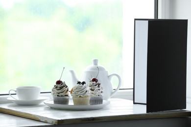 Photo of Cupcakes, tea and light reflector on window sill in studio. Professional food photography