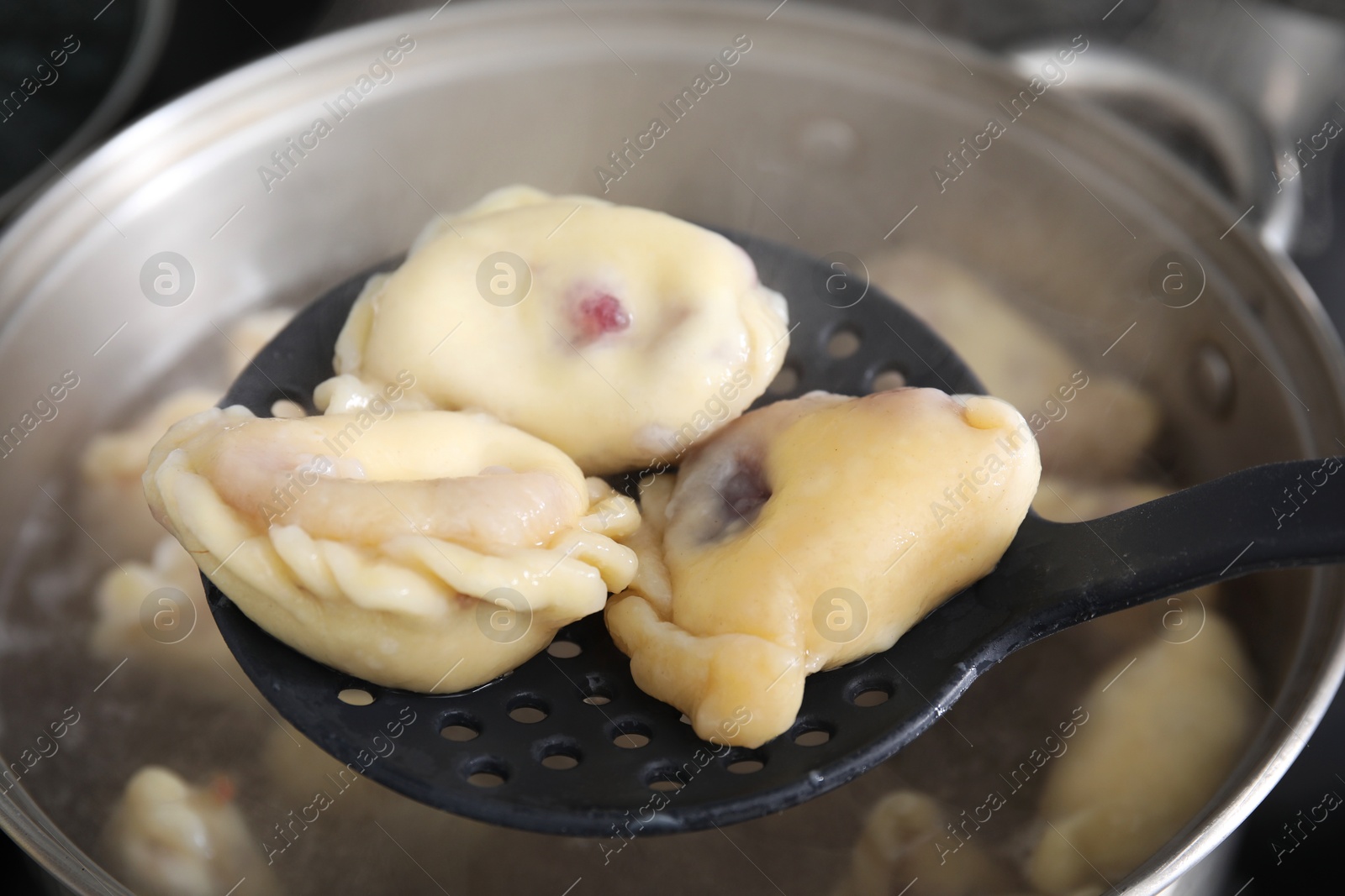 Photo of Preparing varenyky with cherries. Taking dumplings with draining spoon out of pot, closeup