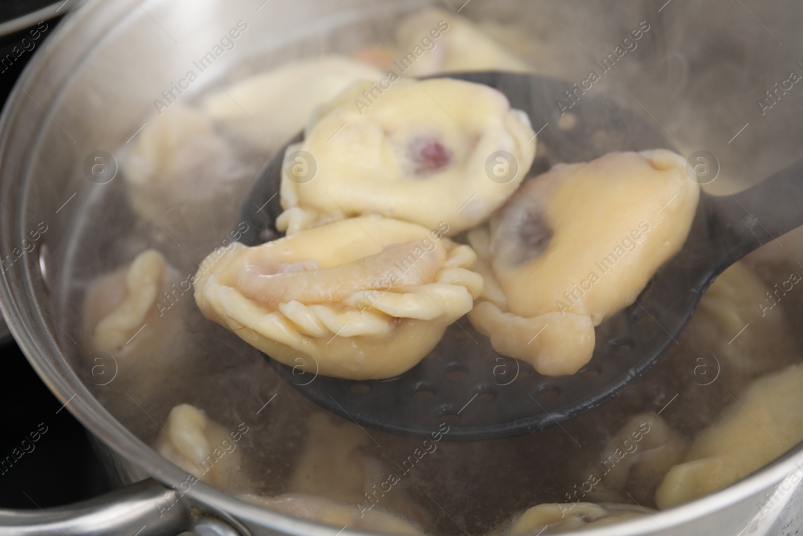 Photo of Preparing varenyky with cherries. Taking dumplings with draining spoon out of pot, closeup