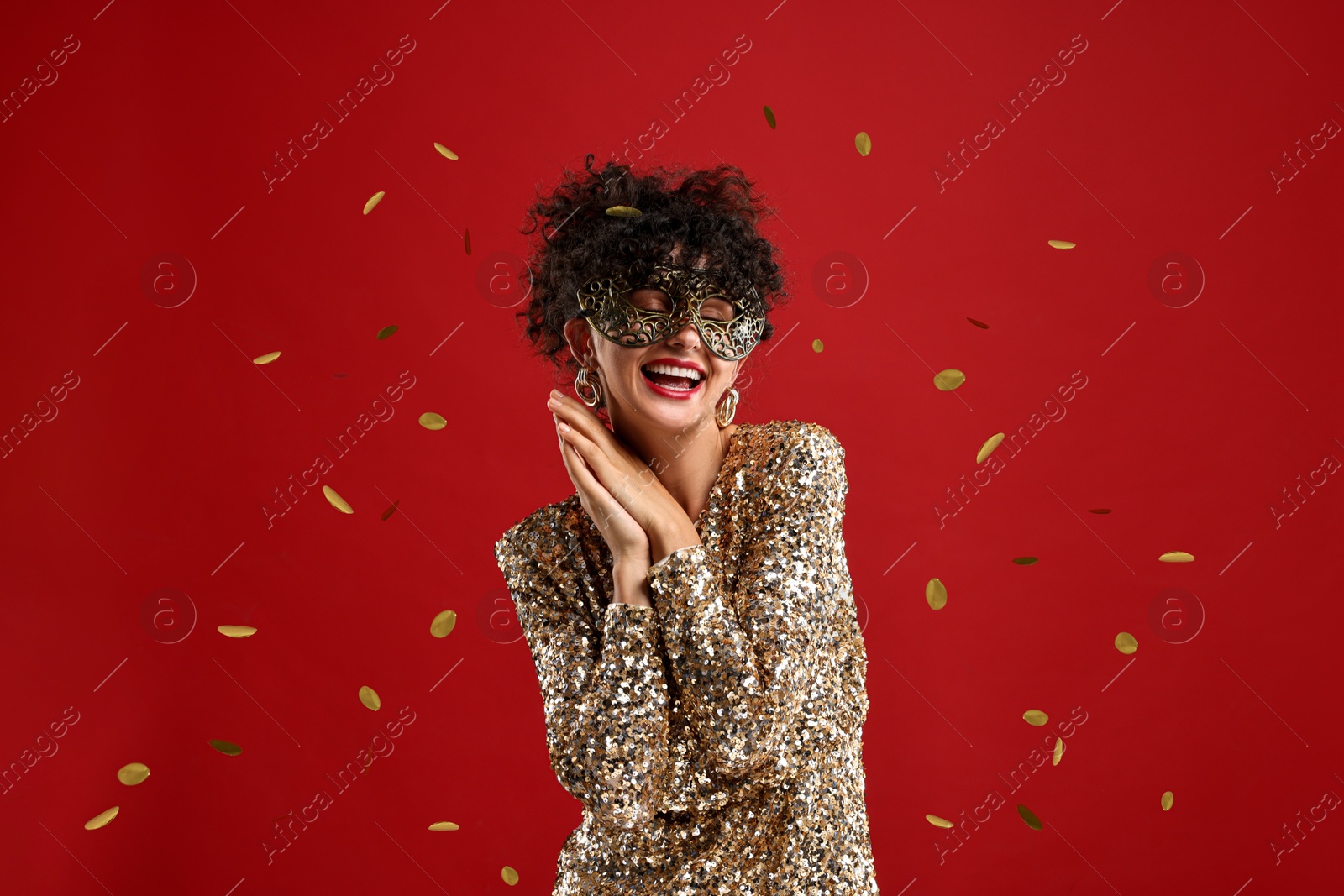 Photo of Happy young woman wearing carnival mask on red background with confetti