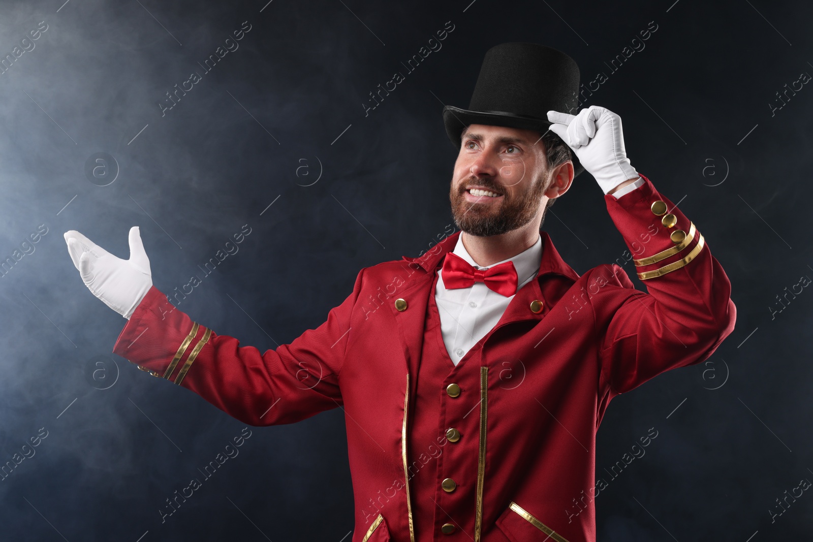 Photo of Portrait of showman in red costume and hat on black background with smoke