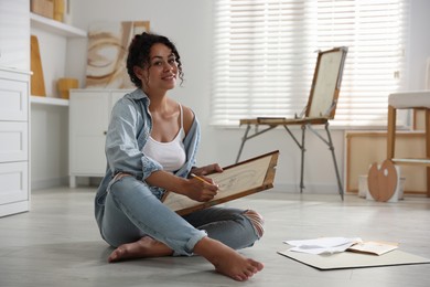 Photo of Smiling woman drawing picture with pencil on floor in studio