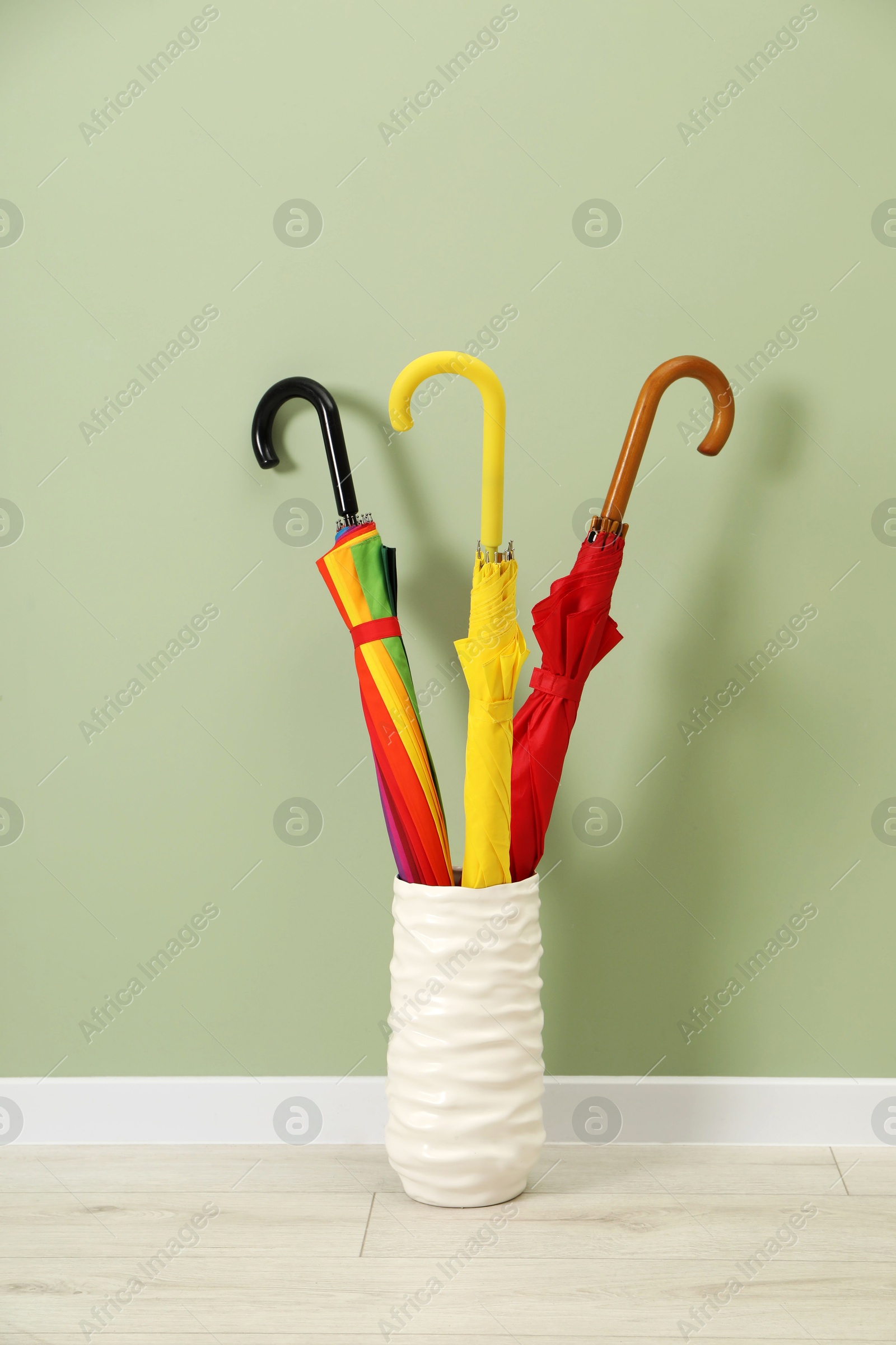 Photo of Colorful umbrellas in holder on floor near green wall indoors