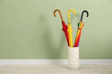 Photo of Colorful umbrellas in holder on floor near green wall indoors, space for text