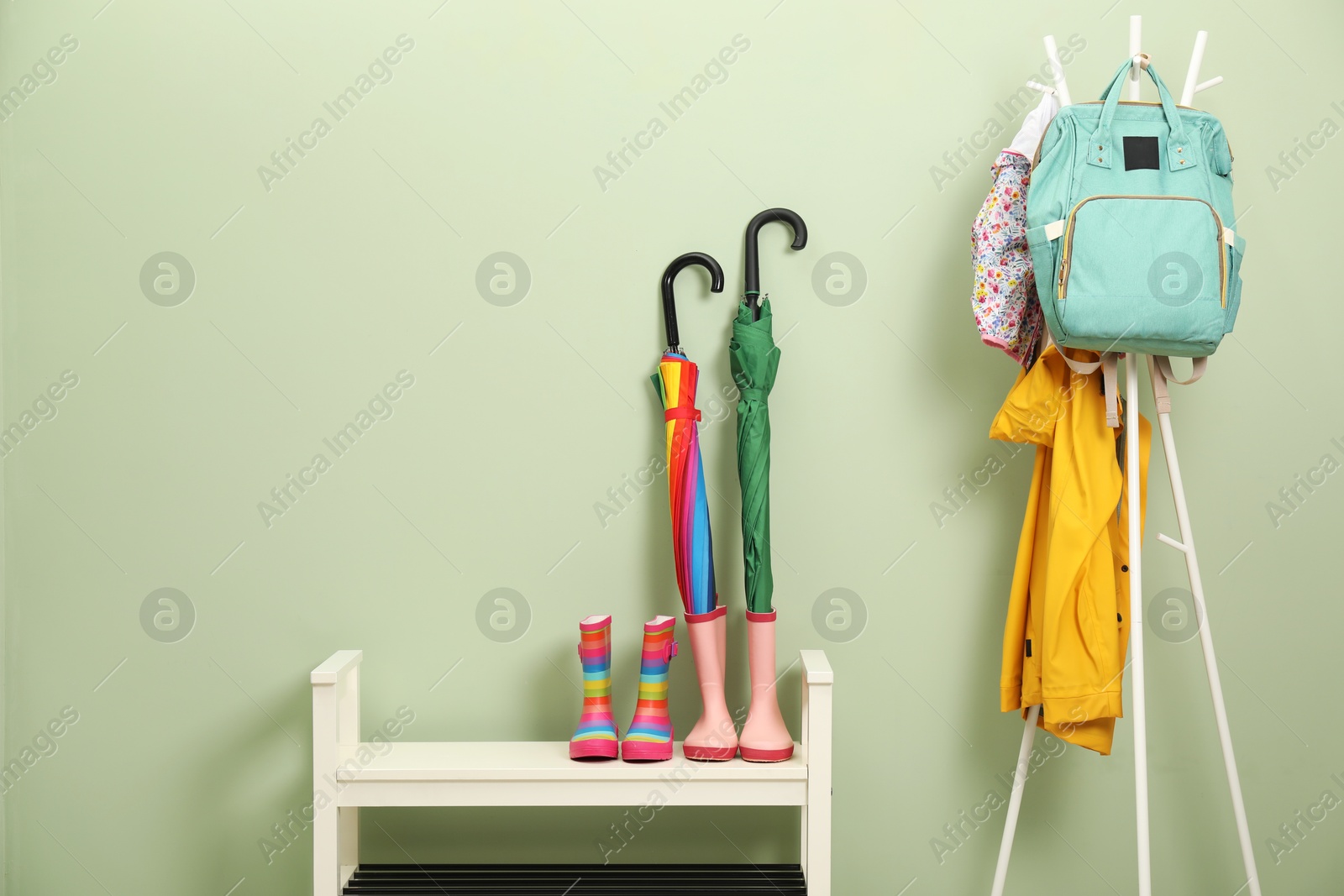 Photo of Colorful umbrellas, rubber boots and rack with jackets, backpack near green wall, space for text