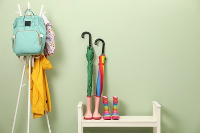 Photo of Colorful umbrellas, rubber boots and rack with jackets, backpack near green wall, space for text