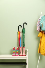 Photo of Colorful umbrellas, rubber boots and rack with jackets, backpack near green wall