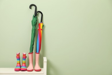 Photo of Colorful umbrellas and rubber boots on bench near green wall, space for text