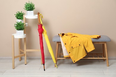 Colorful umbrellas, coat on bench and houseplants near beige wall