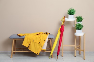 Colorful umbrellas, coat on bench and houseplants near beige wall