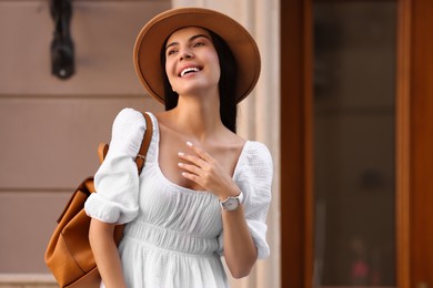 Photo of Beautiful young woman in stylish hat with backpack on city street