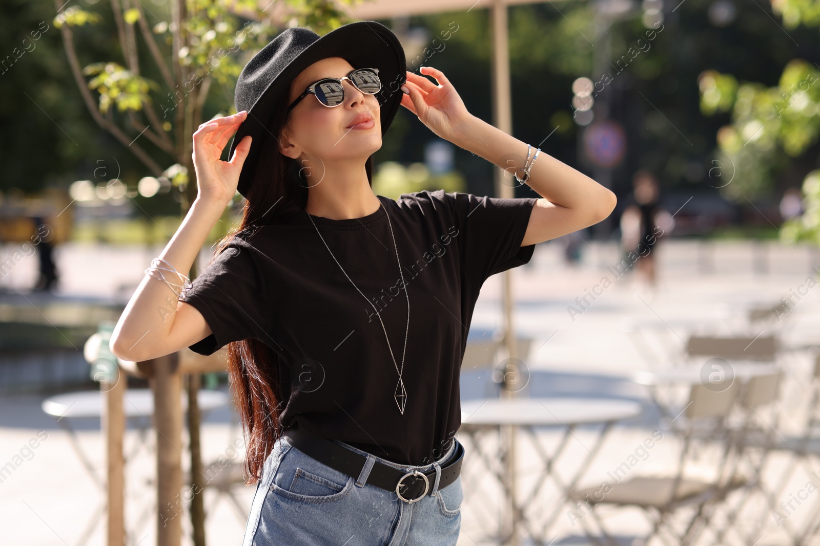 Photo of Young woman in stylish black hat and sunglasses on city street