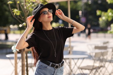 Photo of Young woman in stylish black hat and sunglasses on city street