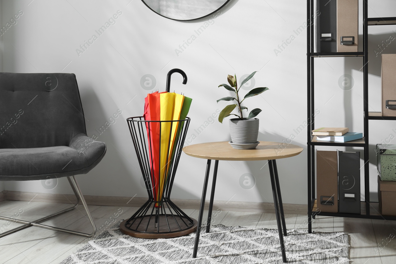 Photo of Colorful umbrella in stand, chair, coffee table and shelving unit indoors